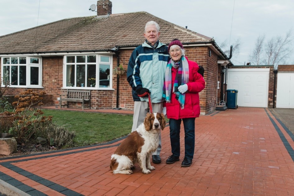 elderly couple and dog smiling outside of their home